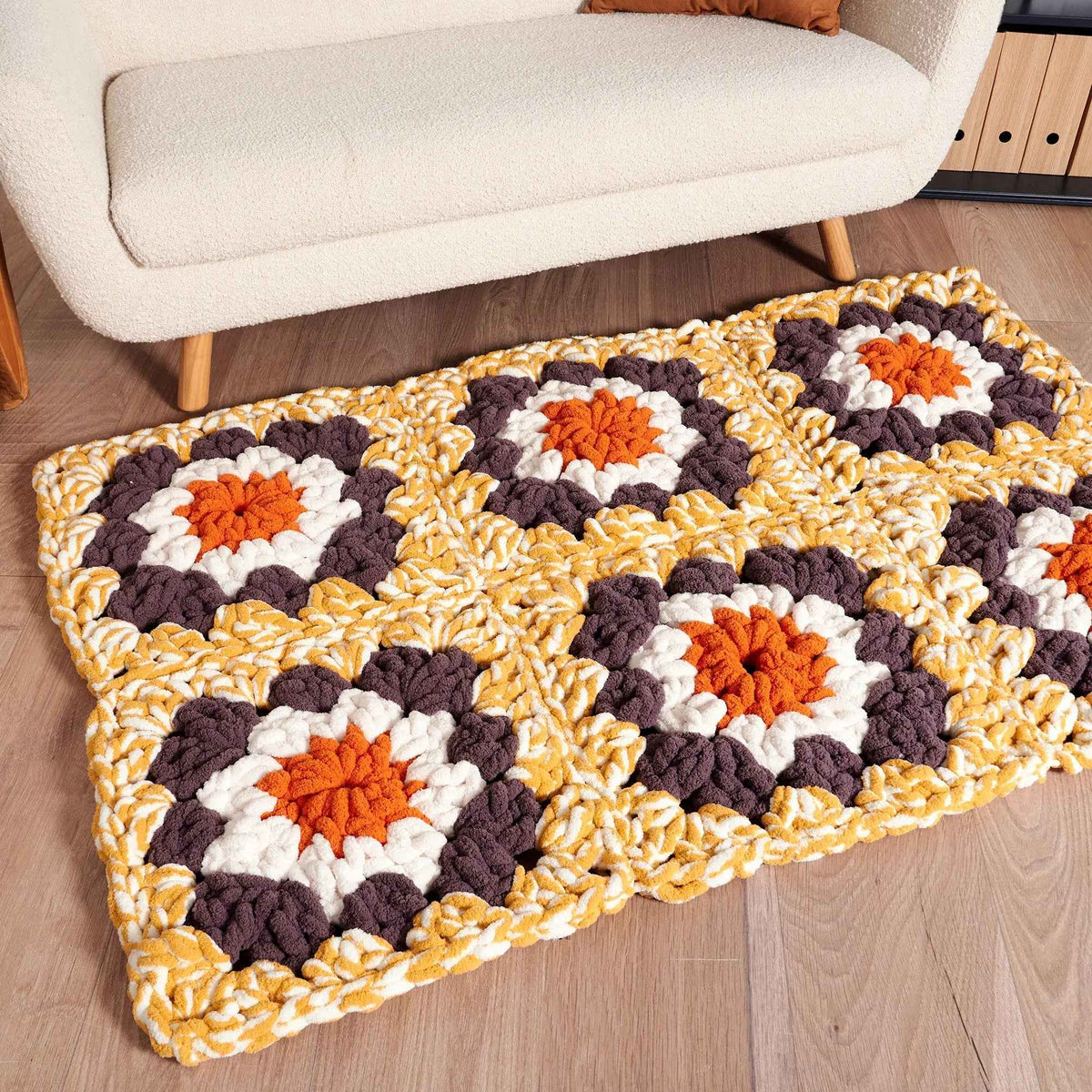 Chunky granny square blanket in orange, yellow, white and brown on a floor