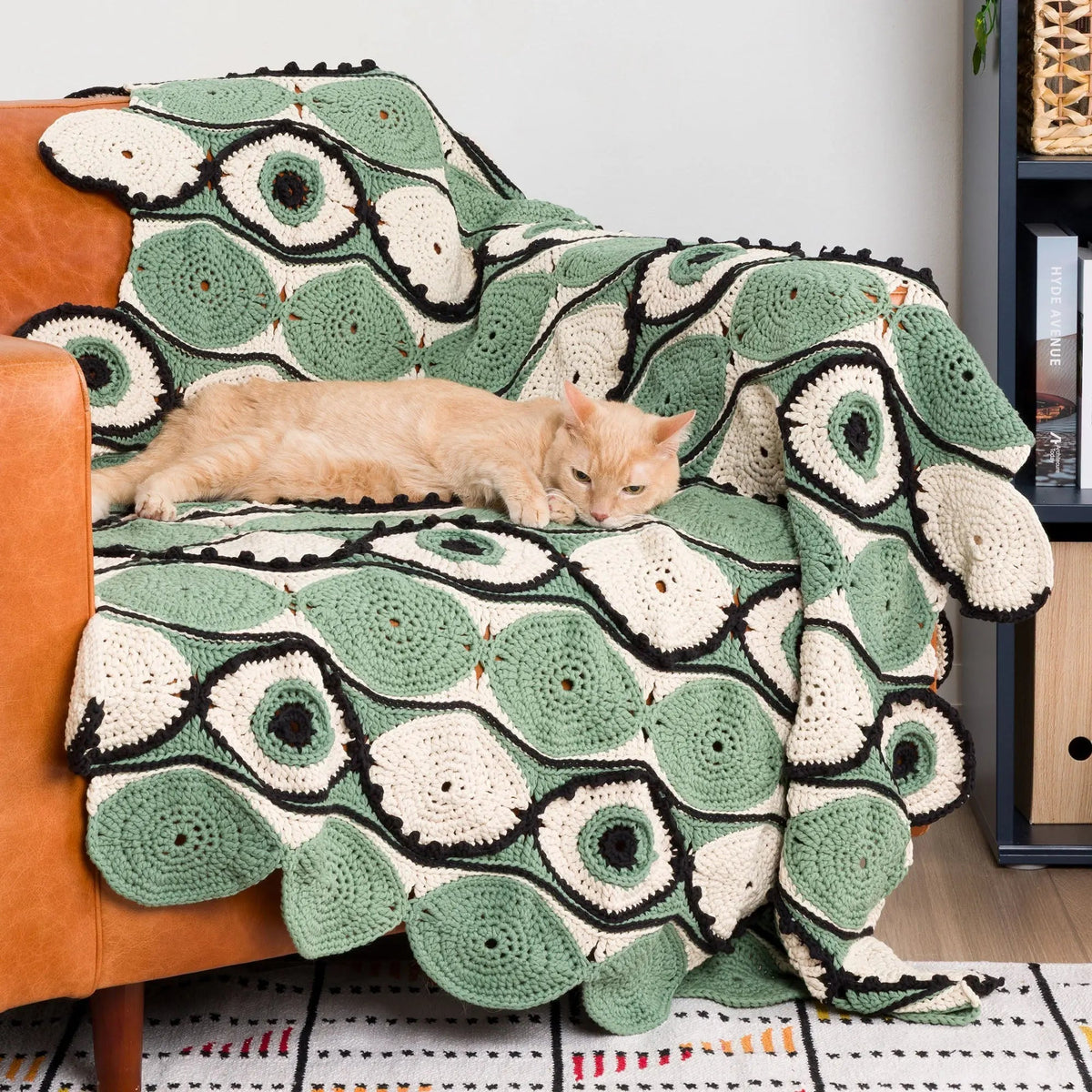 Eye-motif crochet blanket on a chair beside a cat