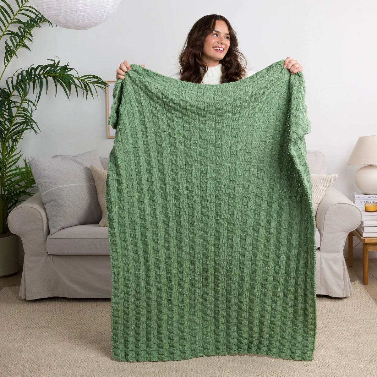 Model holding a green textured knitted blanket