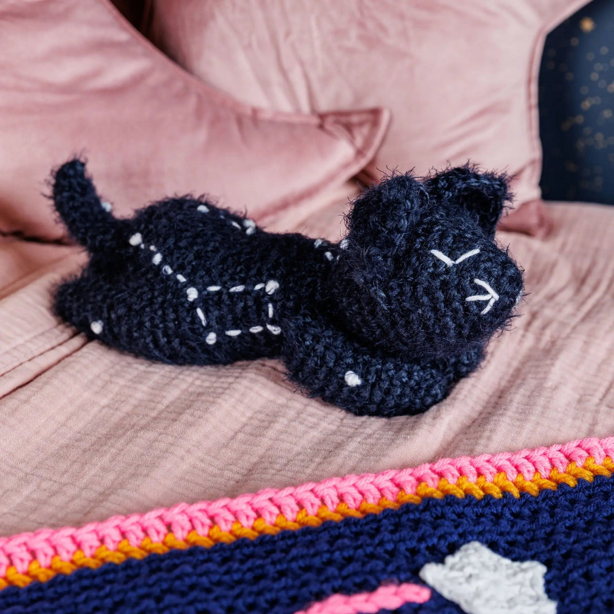 Dark crochet Sleepy Time Kitty resting on pink bedding