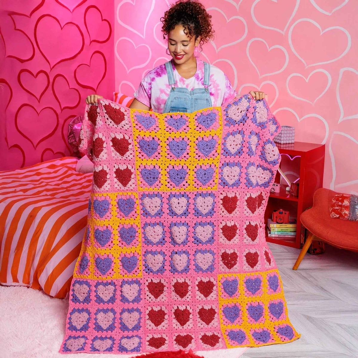 Model holding the pink and purple heart-motif crochet blanket