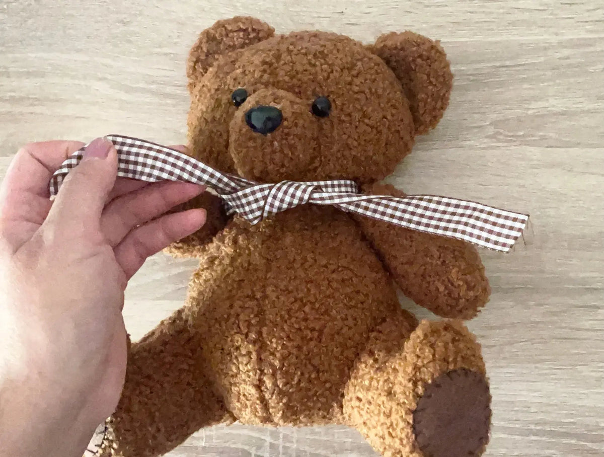 Hand adjusting a gingham bow on a brown teddy bear